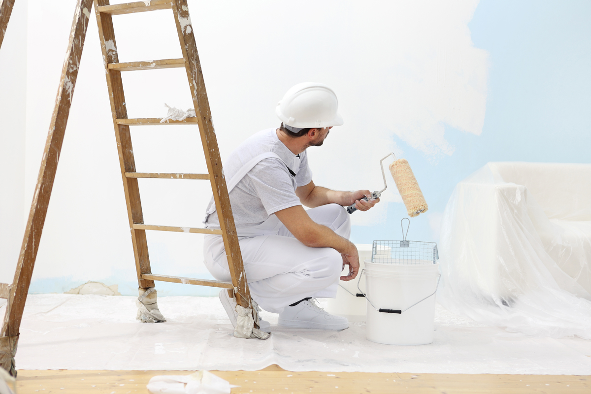 painter man at work takes the color with paint roller from the bucket